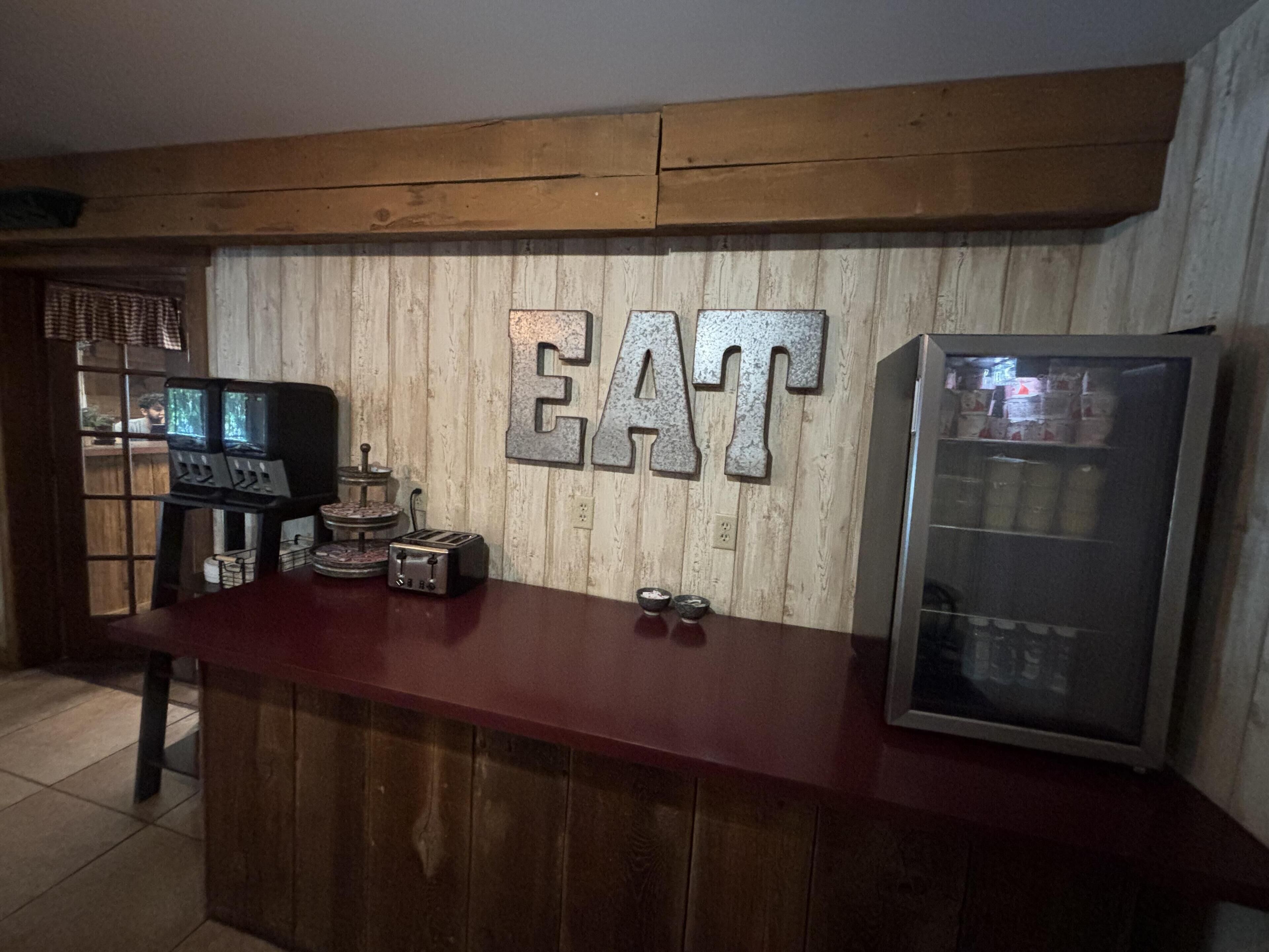 Un comptoir en bois surmonté d’une grande enseigne « À MANGER », une radio d’époque et un réfrigérateur.