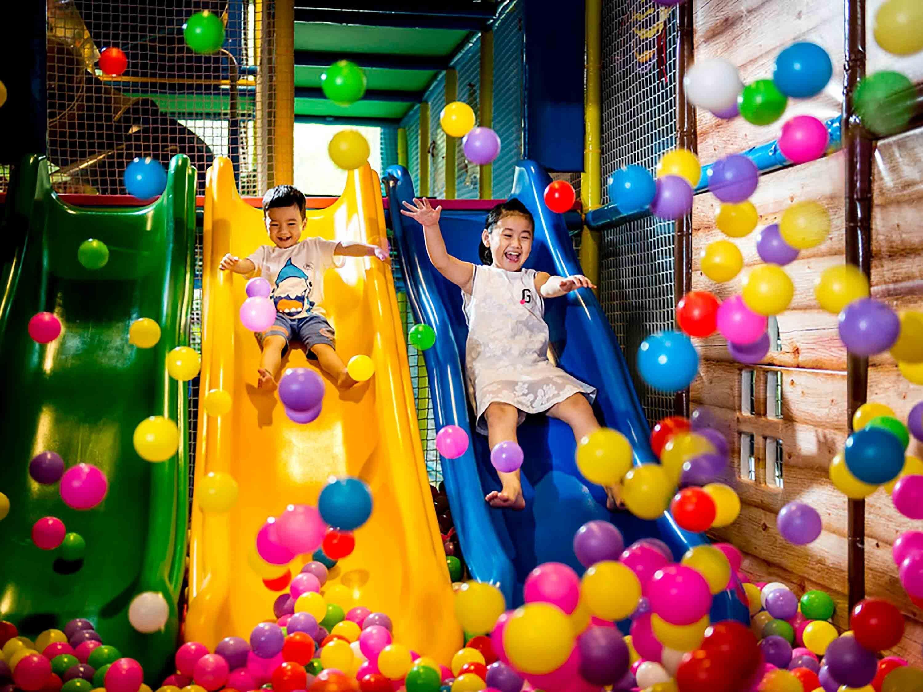 Children sliding down a multi-colored slide in a play area surrounded by colorful balls.