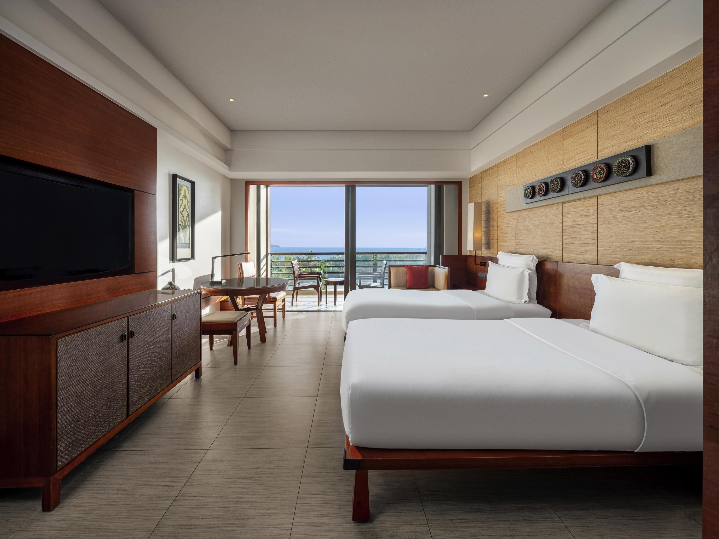 A hotel room with a large TV, a dining area, a bed, and a view of the ocean.