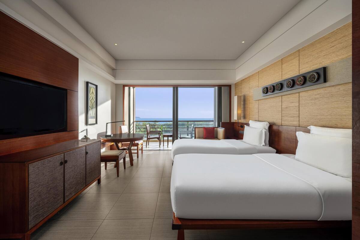 A hotel room with a large TV, a dining area, a bed, and a view of the ocean.