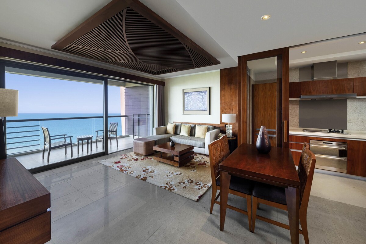 Una sala de estar moderna con un balcón con vista al mar, un comedor y una cocina con electrodomésticos de acero inoxidable.