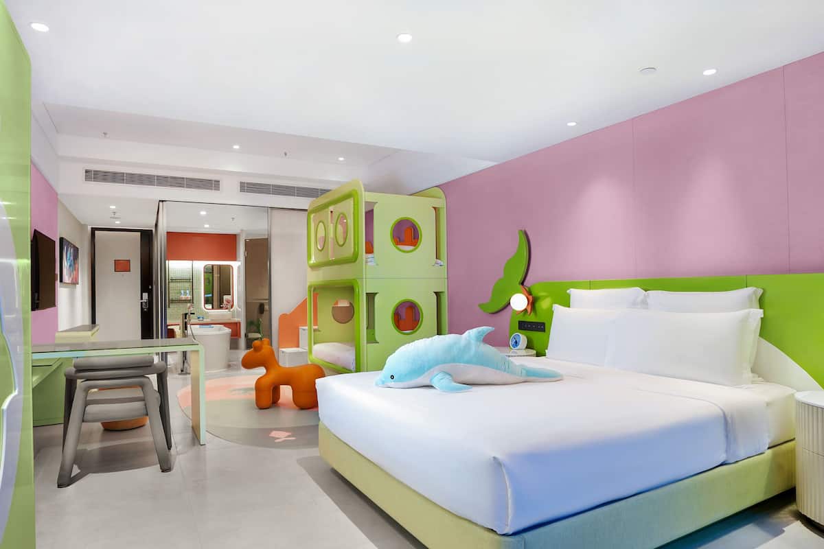 Quarto de hotel moderno com uma cama, uma escrivaninha e um banheiro visível por uma porta aberta.