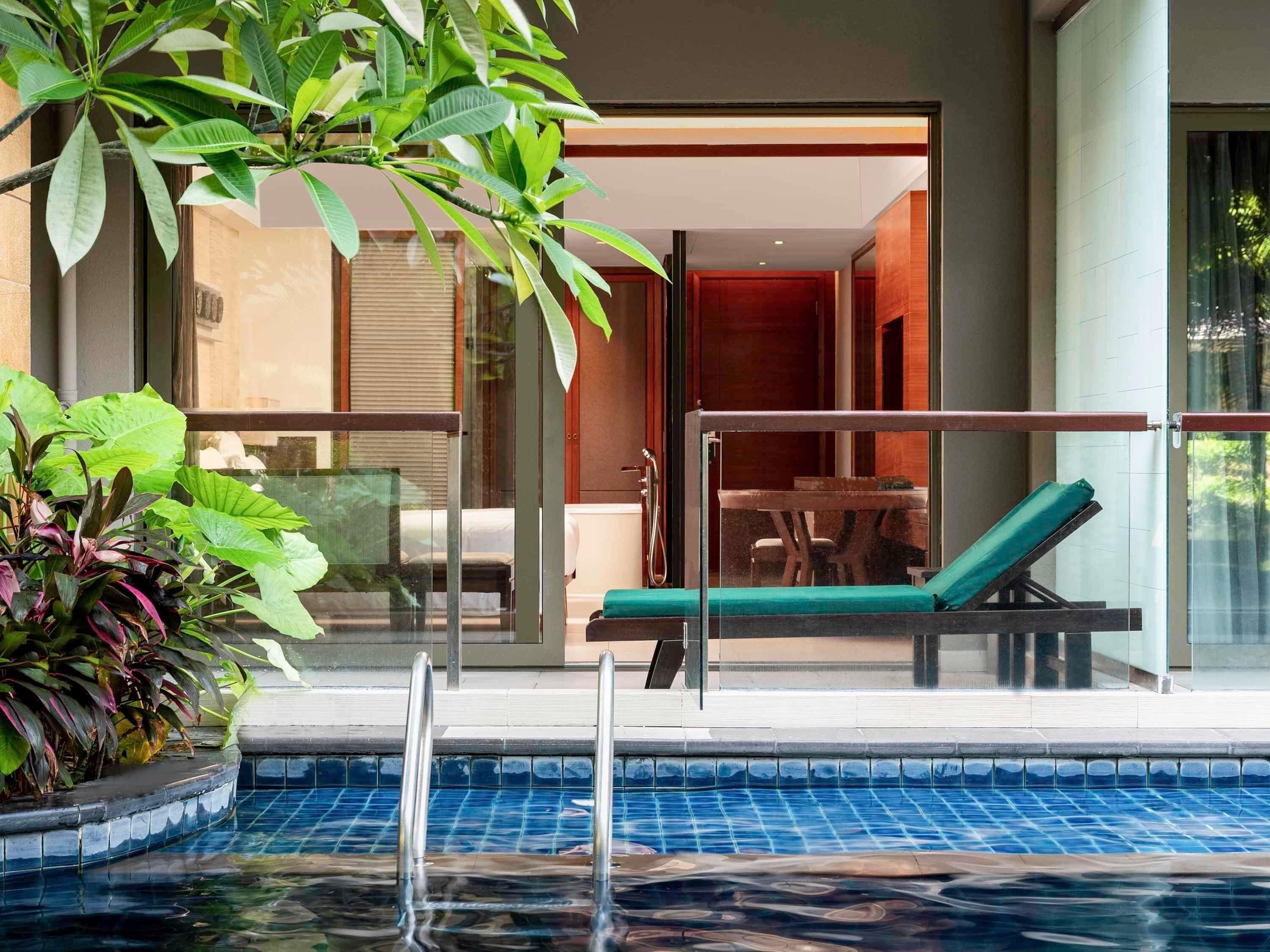 A pool area with a lounge chair, a glass balustrade, and potted plants.