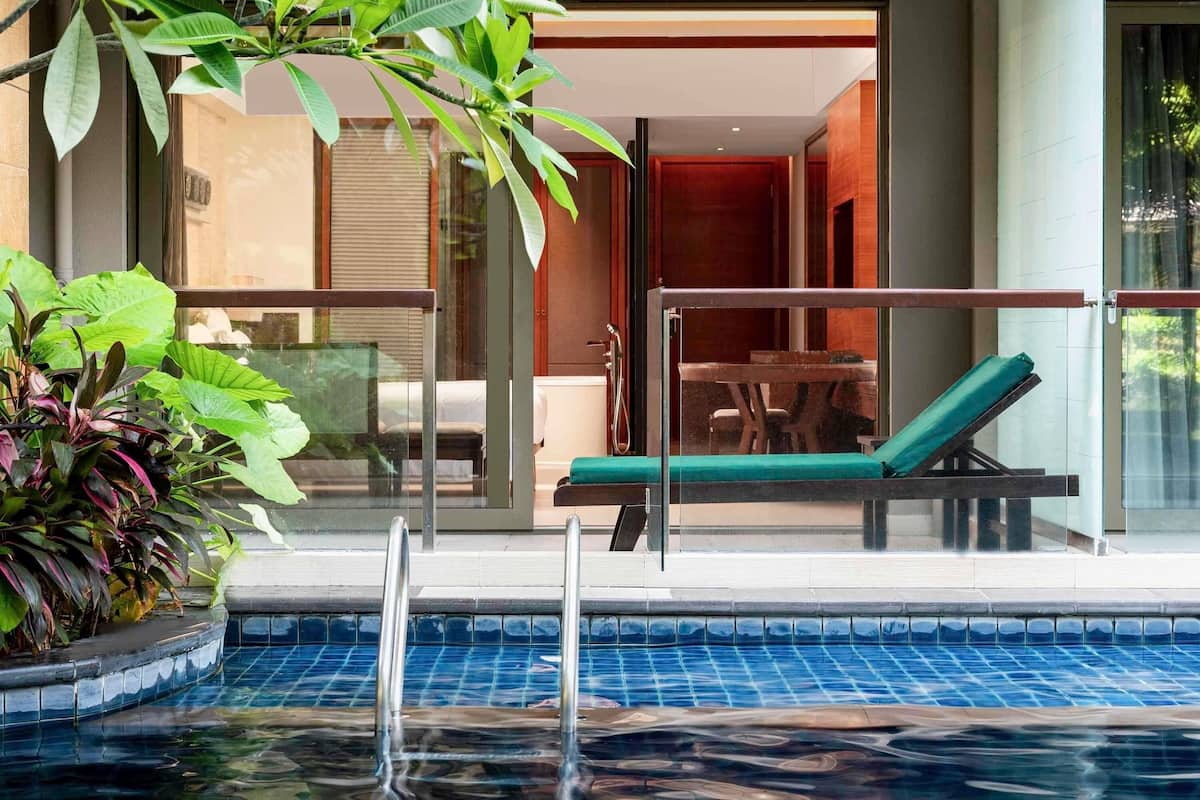 A pool area with a lounge chair, a glass balustrade, and potted plants.