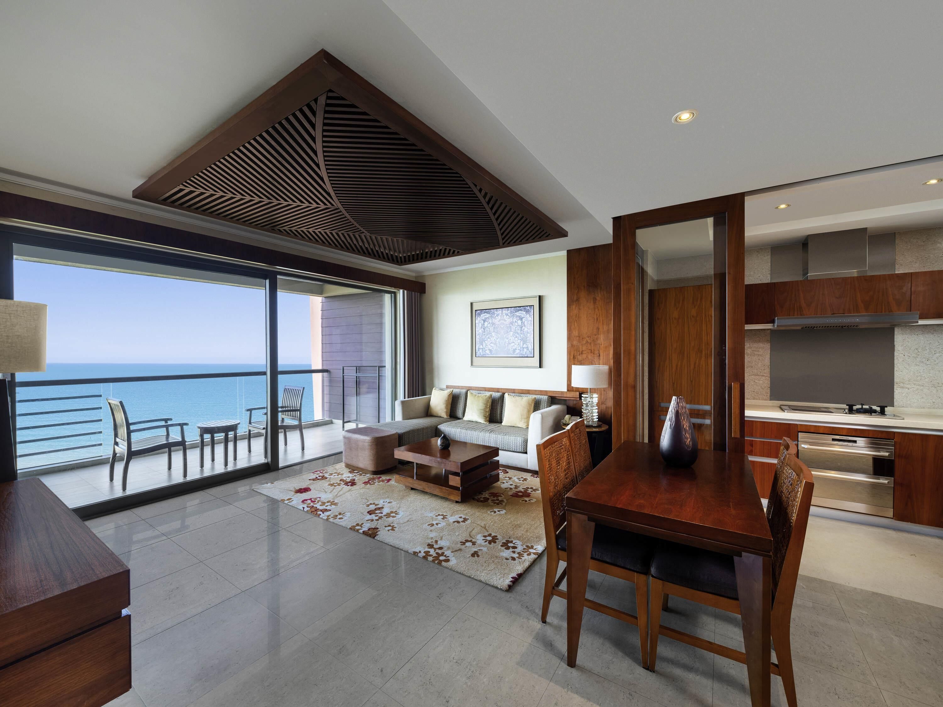 A modern living room with a balcony overlooking the sea, a dining area, and a kitchen with stainless steel appliances.