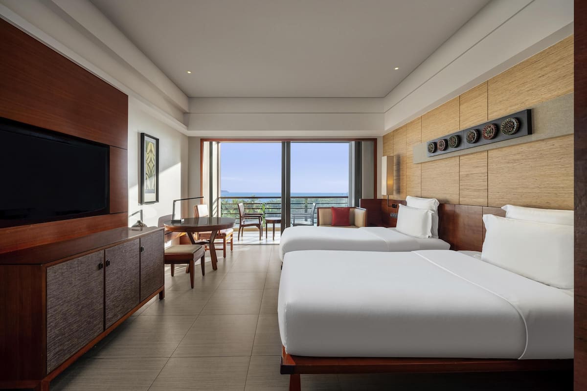 A hotel room with a large TV, a dining area, a bed, and a view of the ocean.