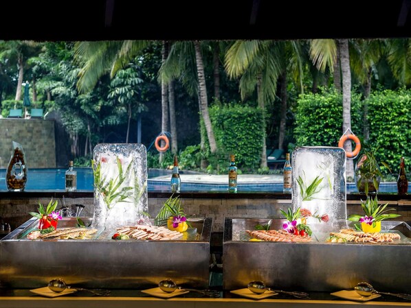 A bar area with a pool view, featuring two large ice glasses with tropical plants, a selection of seafood, and a tropical setting with palm trees and a pool in the background. - Pullman Oceanview Sanya Bay Resort & Spa (Sanya)