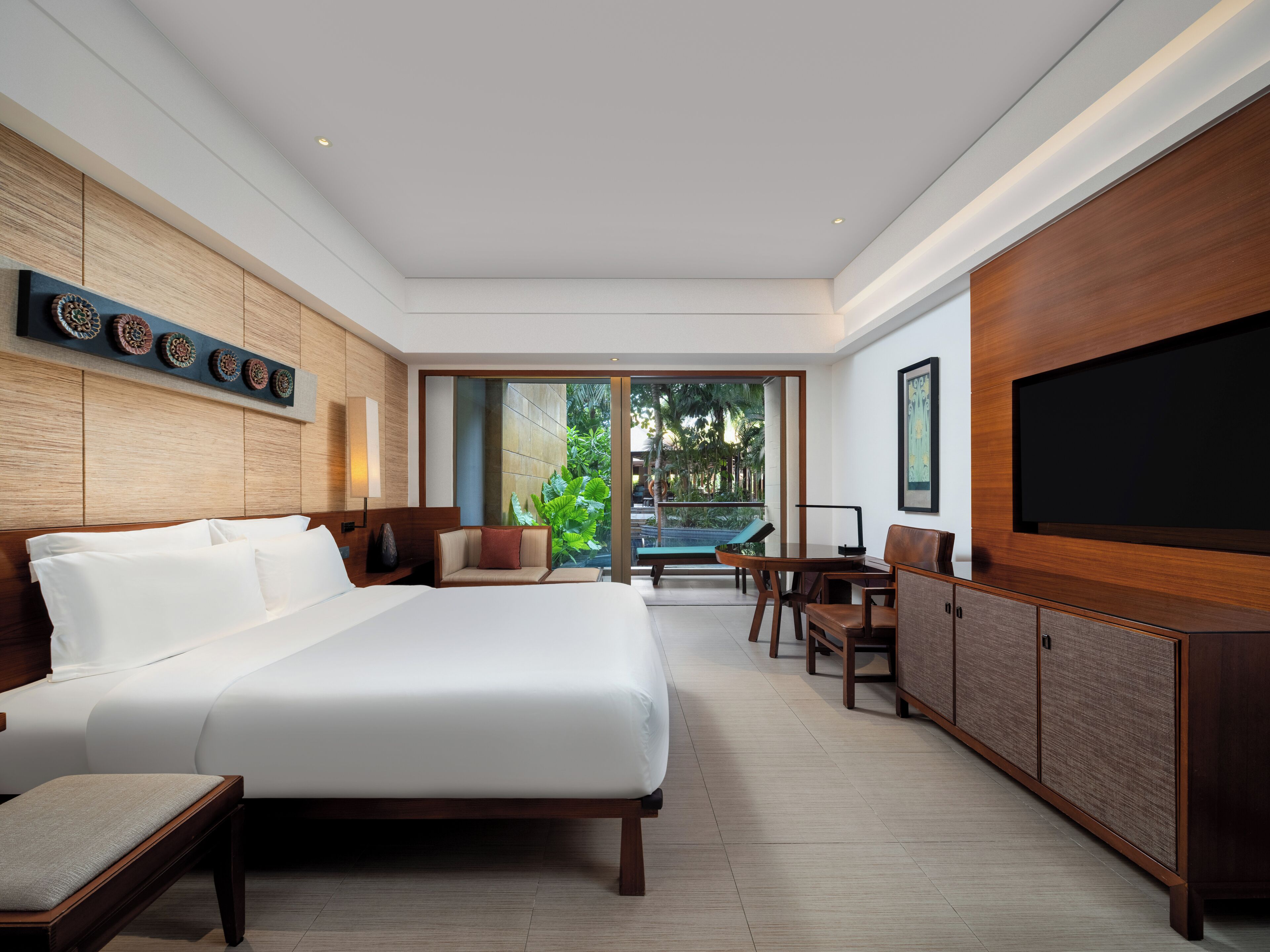A modern hotel room with a large bed, a seating area with a view of the outdoors, and a flat-screen TV.