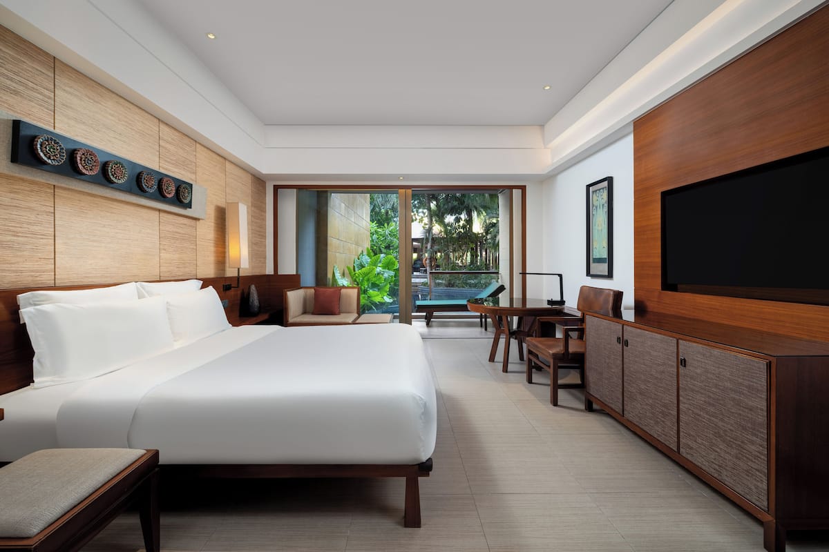 A modern hotel room with a large bed, a seating area with a view of the outdoors, and a flat-screen TV.