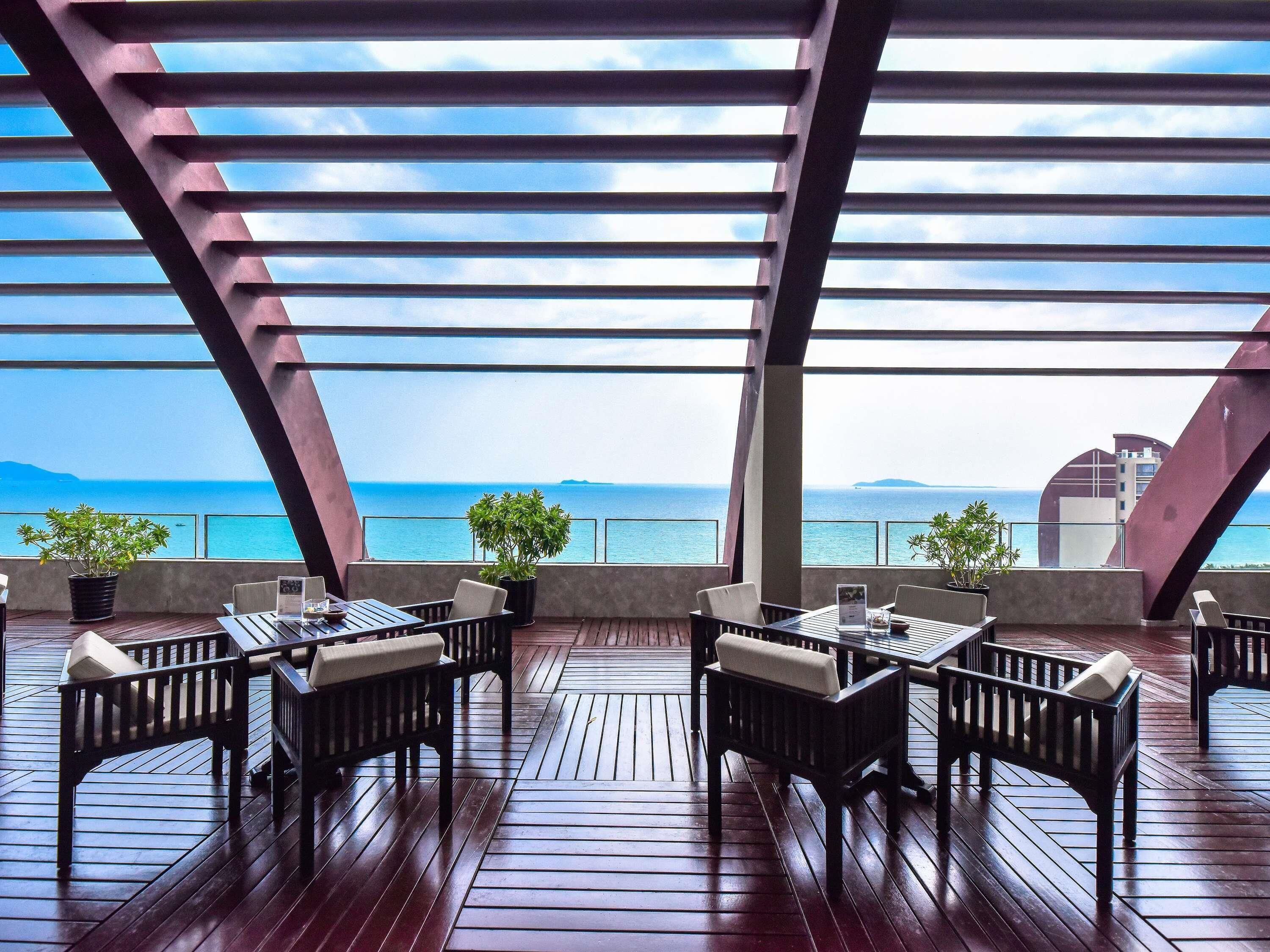 Un espace extérieur aménagé pour les repas, avec des tables et des chaises en bois, des plantes en pot et une vue sur la mer.
