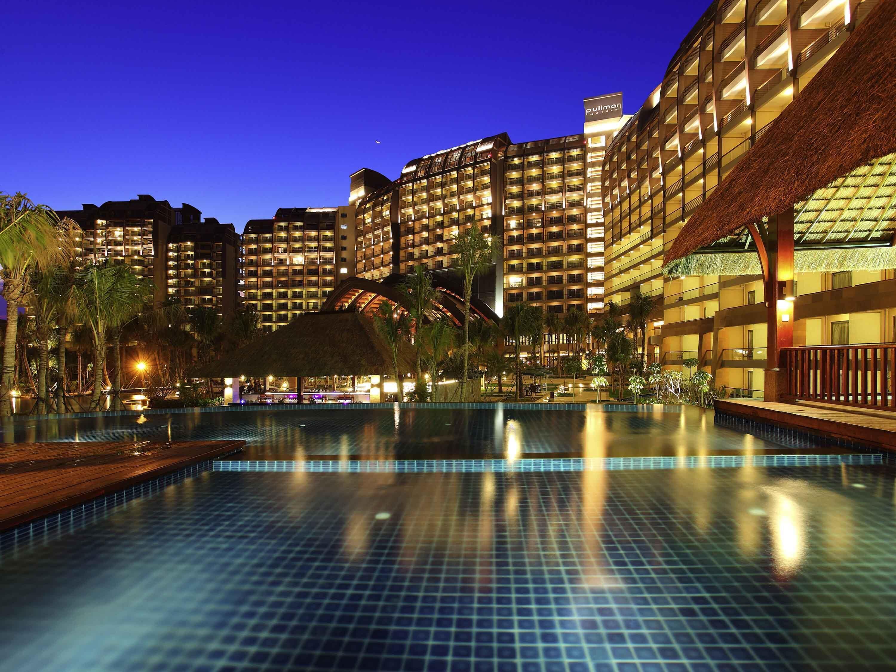 A hotel with multiple high-rise buildings, a swimming pool, and a thatched-roof structure.