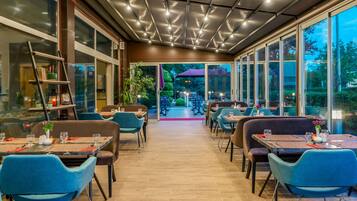 An indoor dining area with tables and chairs, a ceiling with lights, and large windows.