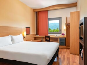 A hotel room with a bed, desk, chair, TV, and a view of mountains. - ibis Bursa (Bursa)