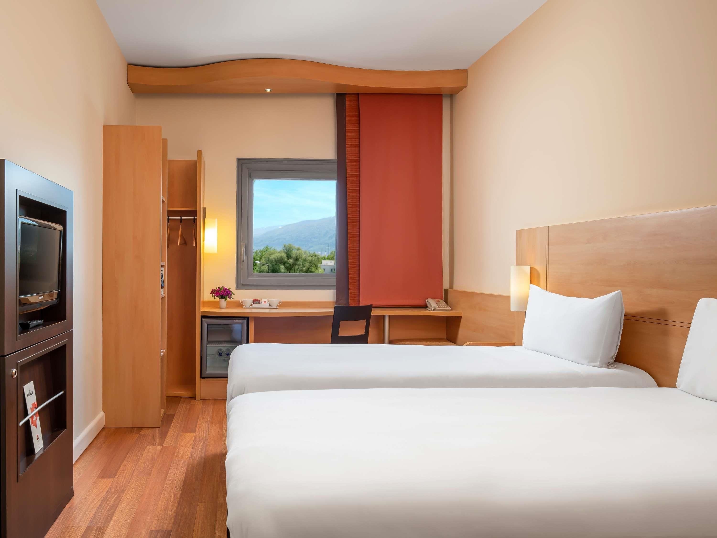 Habitación de hotel con dos camas, un escritorio con silla, televisión, ventana con vistas y minibar.