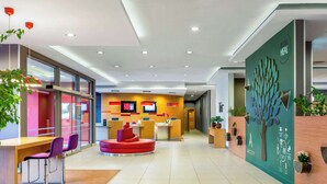 A modern reception area with a central red seating area, a reception desk, and a wall-mounted digital display. - ibis Bursa (Bursa)