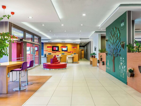 A modern reception area with a central red seating area, a reception desk, and a wall-mounted digital display. - ibis Bursa (Bursa)