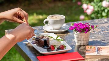 A person dining outdoors with a plate of food, a cup of coffee, and a book on a table.