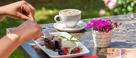 A person dining outdoors with a plate of food, a cup of coffee, and a book on a table.