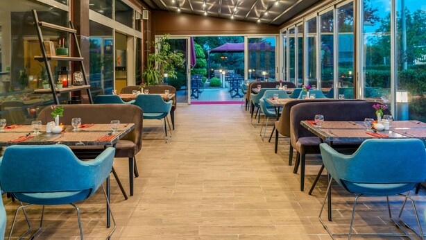 An indoor dining area with tables and chairs, a ceiling with lights, and large windows. - ibis Bursa (Bursa)