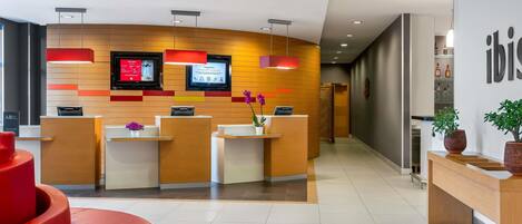 A modern reception area with a wooden reception desk, two monitors, and a red accent wall.