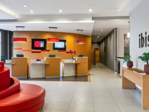 Una moderna zona de recepción con un mostrador de madera, dos monitores y una pared de acento roja.