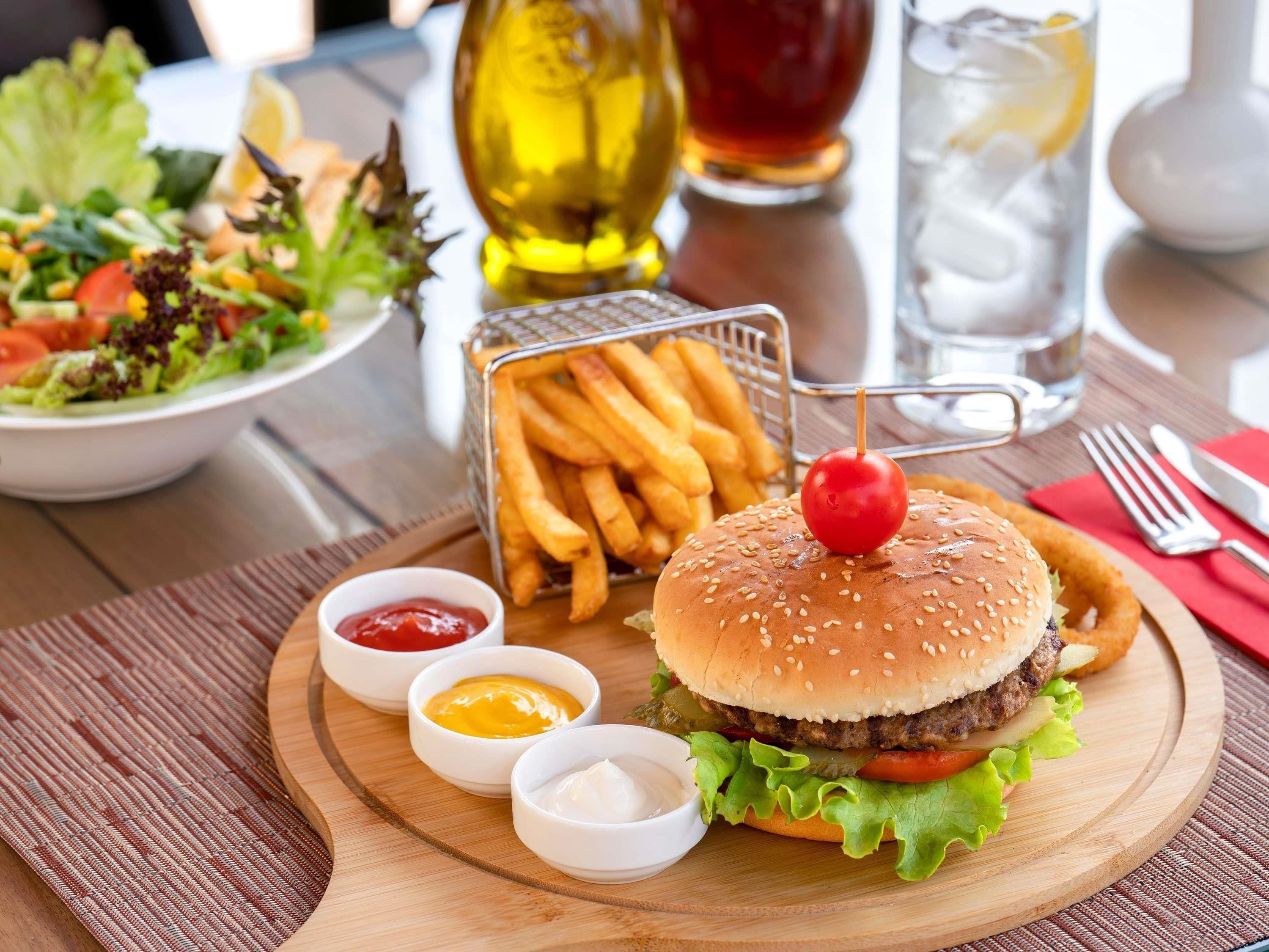 A meal with a burger, fries, salad, and condiments on a wooden board.