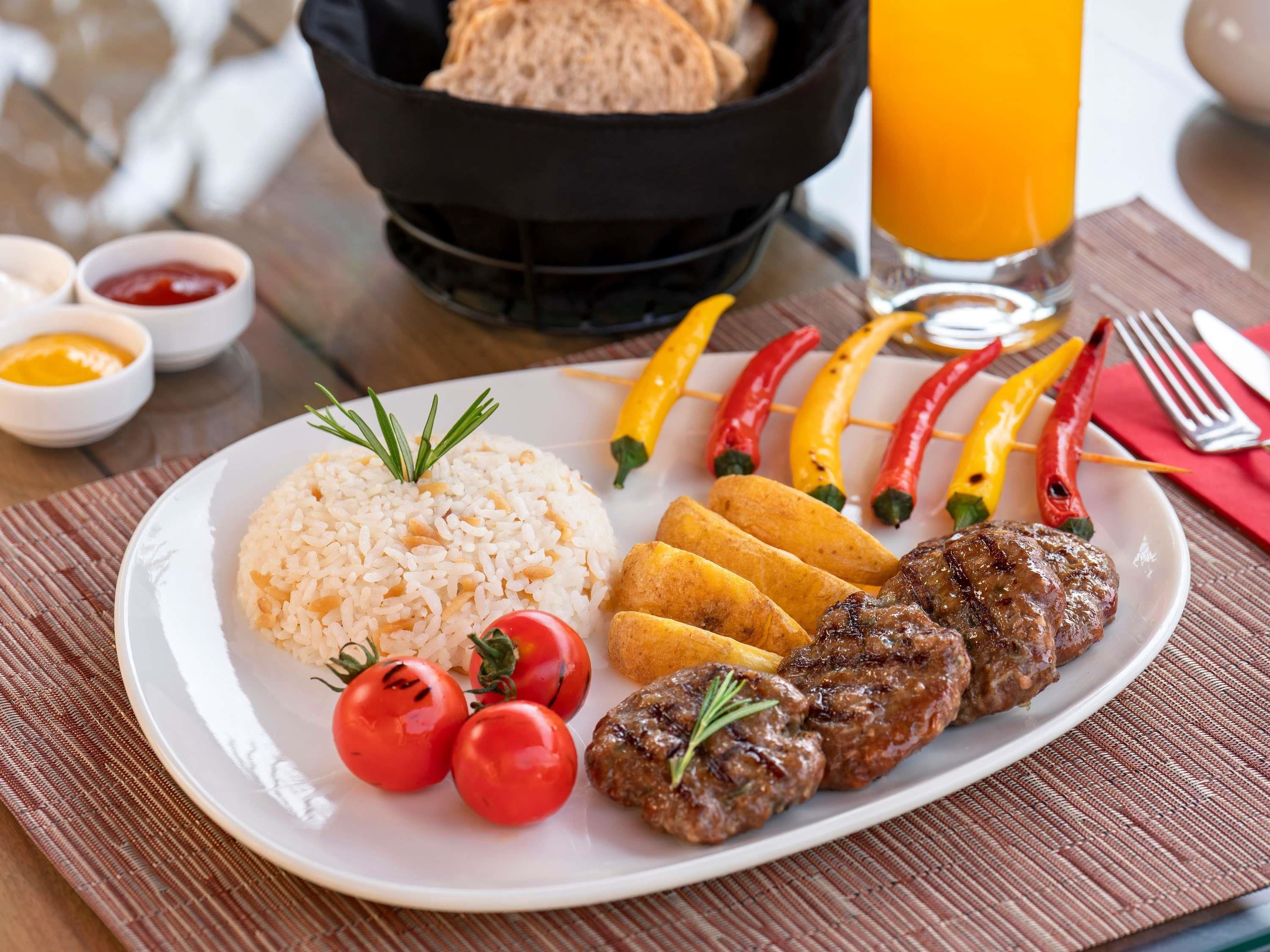 Une assiette de riz, de viande grillée, de tomates et de poivrons grillés.