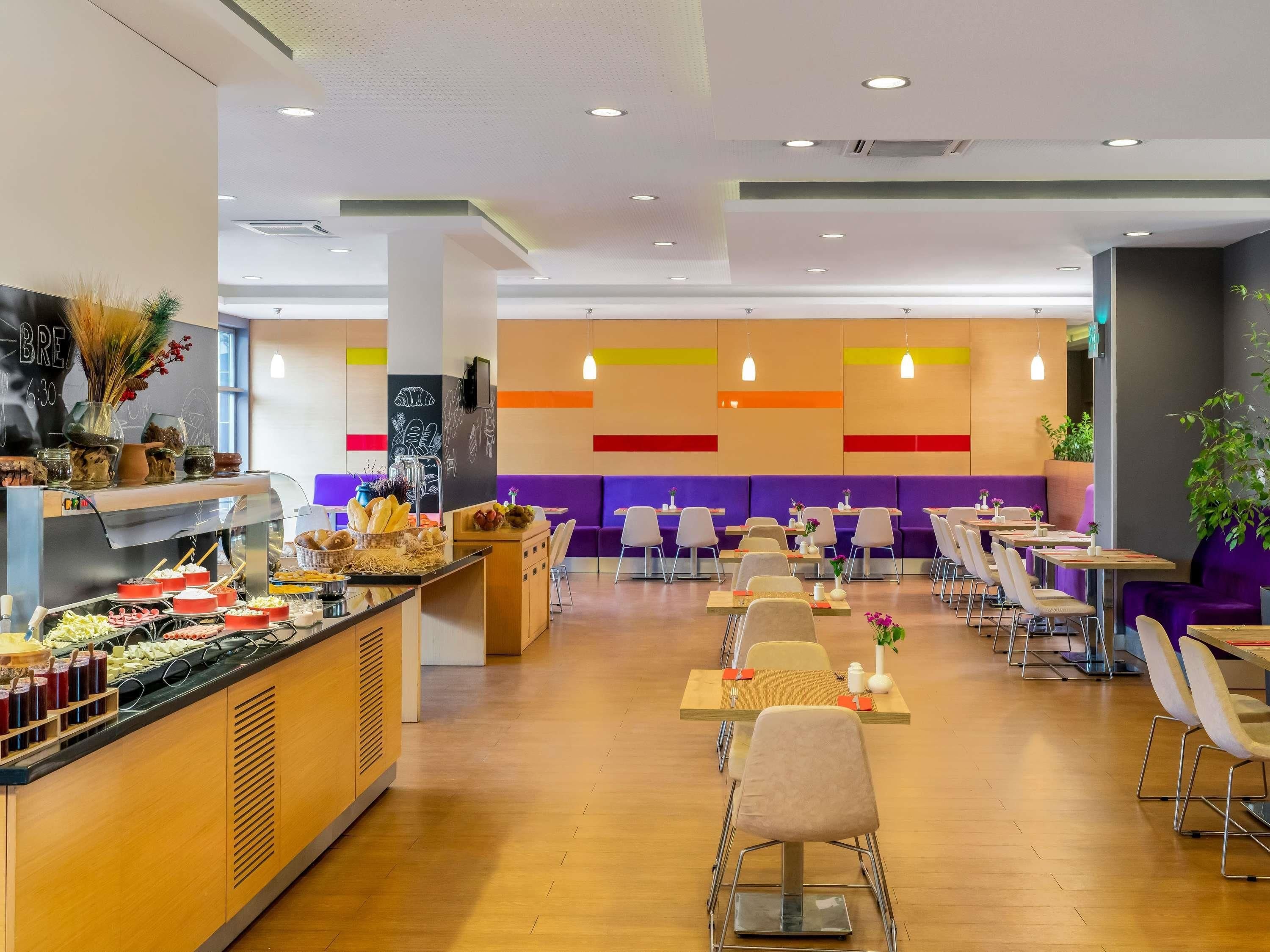 Una cafetería moderna con mostrador central, zona de asientos y pared con paneles de colores.