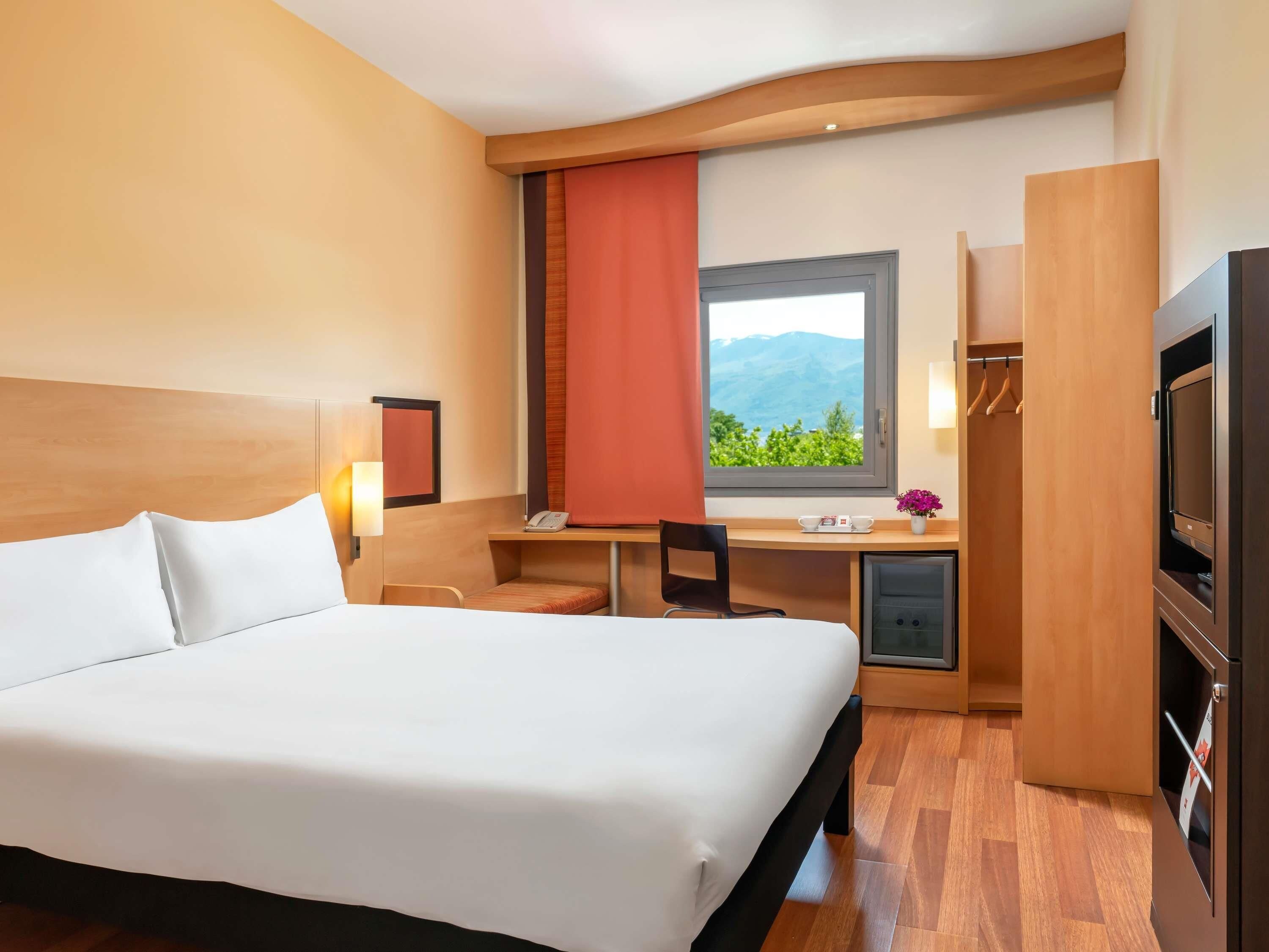 Habitación de hotel con una cama grande, un escritorio con silla, televisor y armario.
