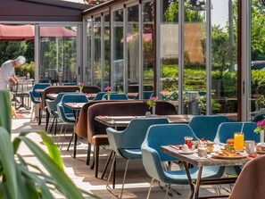 An outdoor dining area with tables and chairs, large windows, and a view of greenery. - ibis Bursa (Bursa)