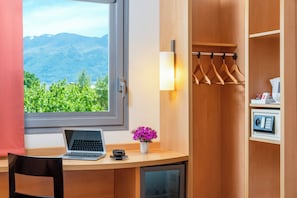 A room with a desk, laptop, and a view of mountains through a window.