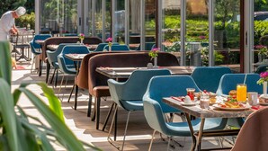 An outdoor dining area with tables and chairs, large windows, and a view of greenery. - ibis Bursa (Bursa)