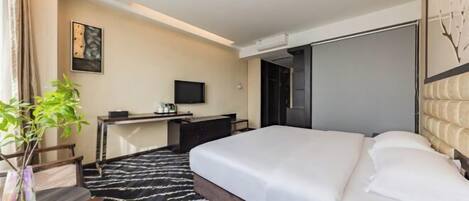 Une chambre d’hôtel avec un grand lit, un bureau, une chaise, une télévision et une plante.