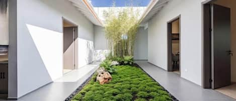 Un interior moderno con un jardín central, una escalera y una puerta que conduce a otra habitación.