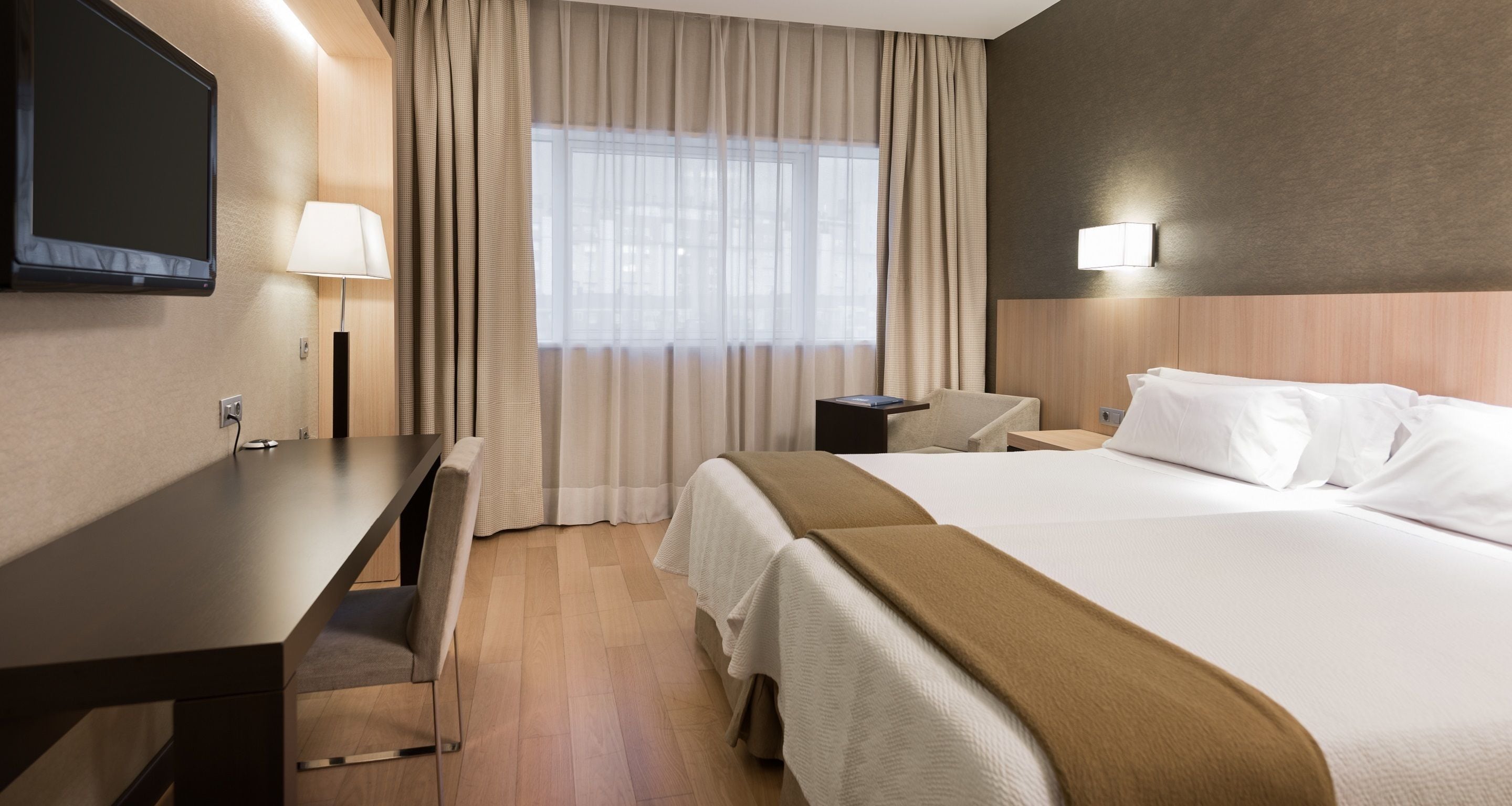 Hotelkamer met een bed, bureau, stoel, televisie en raam met gordijnen.