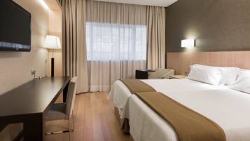 Hotelkamer met een bed, bureau, stoel, televisie en raam met gordijnen.