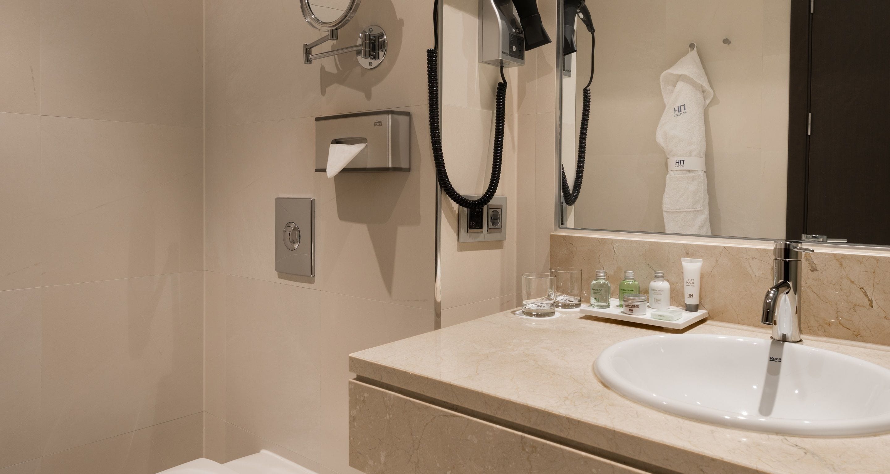 Un baño moderno con lavamanos, espejo, toallero y secador de pelo.
