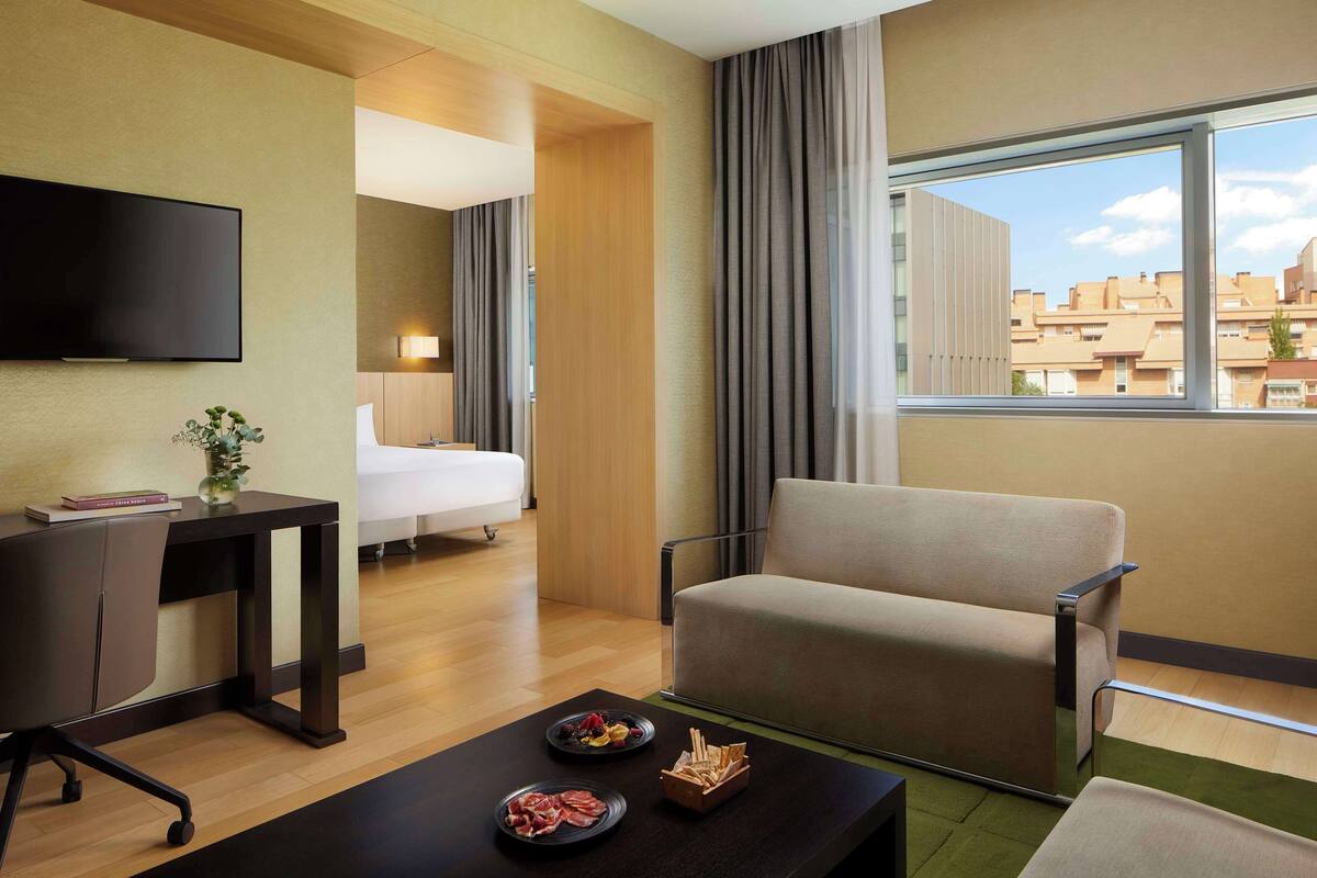 Habitación de hotel con cama, televisor, escritorio con silla, sofá y mesa de comedor con comida.