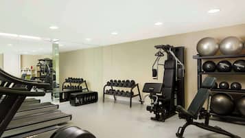 Un gimnasio con cintas de correr, mancuernas, prensa de banca y pelotas de ejercicio.