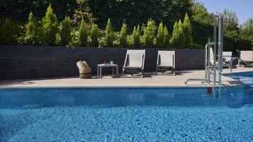Una piscina con agua cristalina azul, rodeada de sillas de descanso y un muro de piedra.