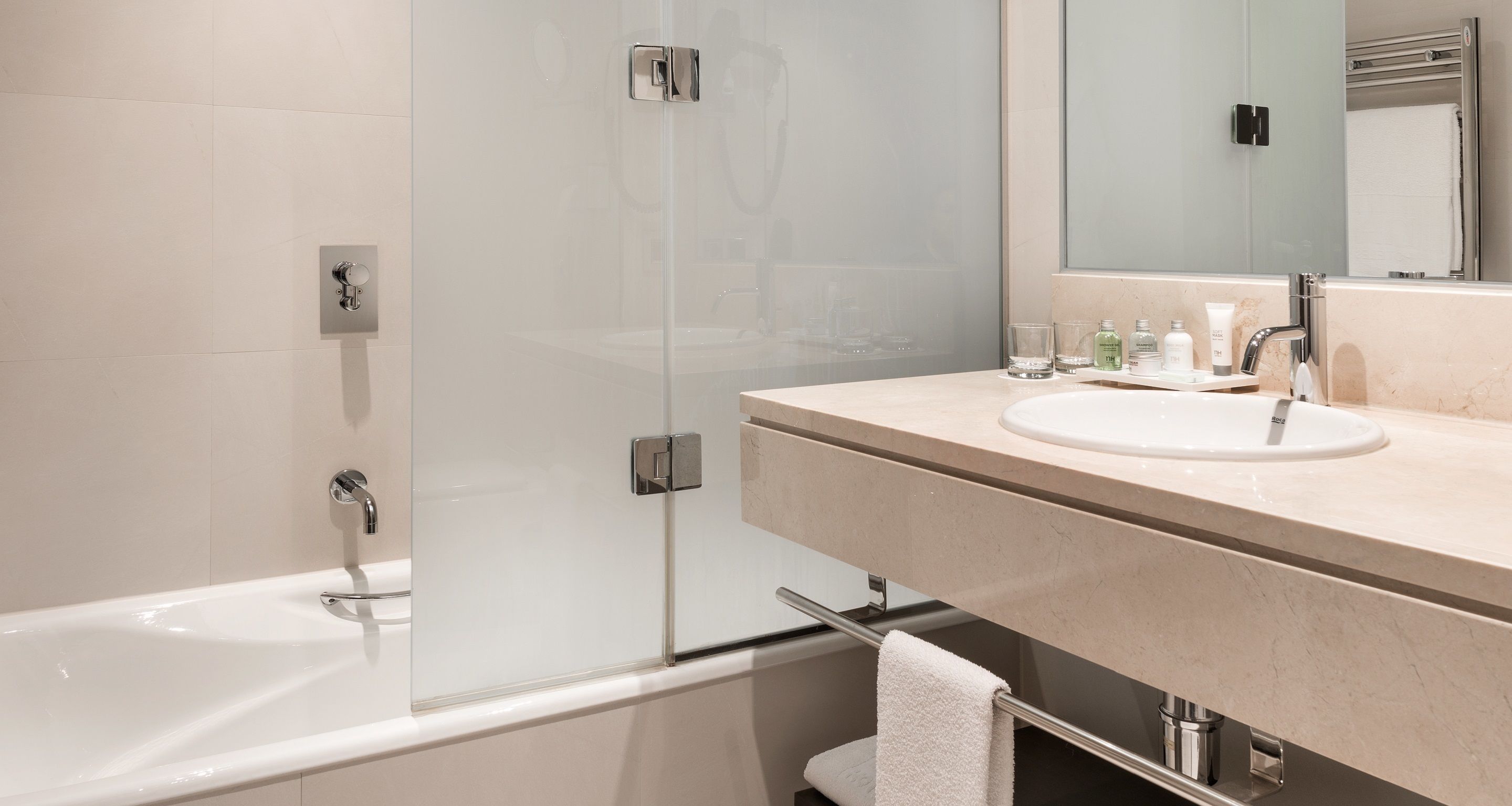A modern bathroom with a glass-enclosed shower, a white bathtub, and a beige vanity with a sink and mirror.
