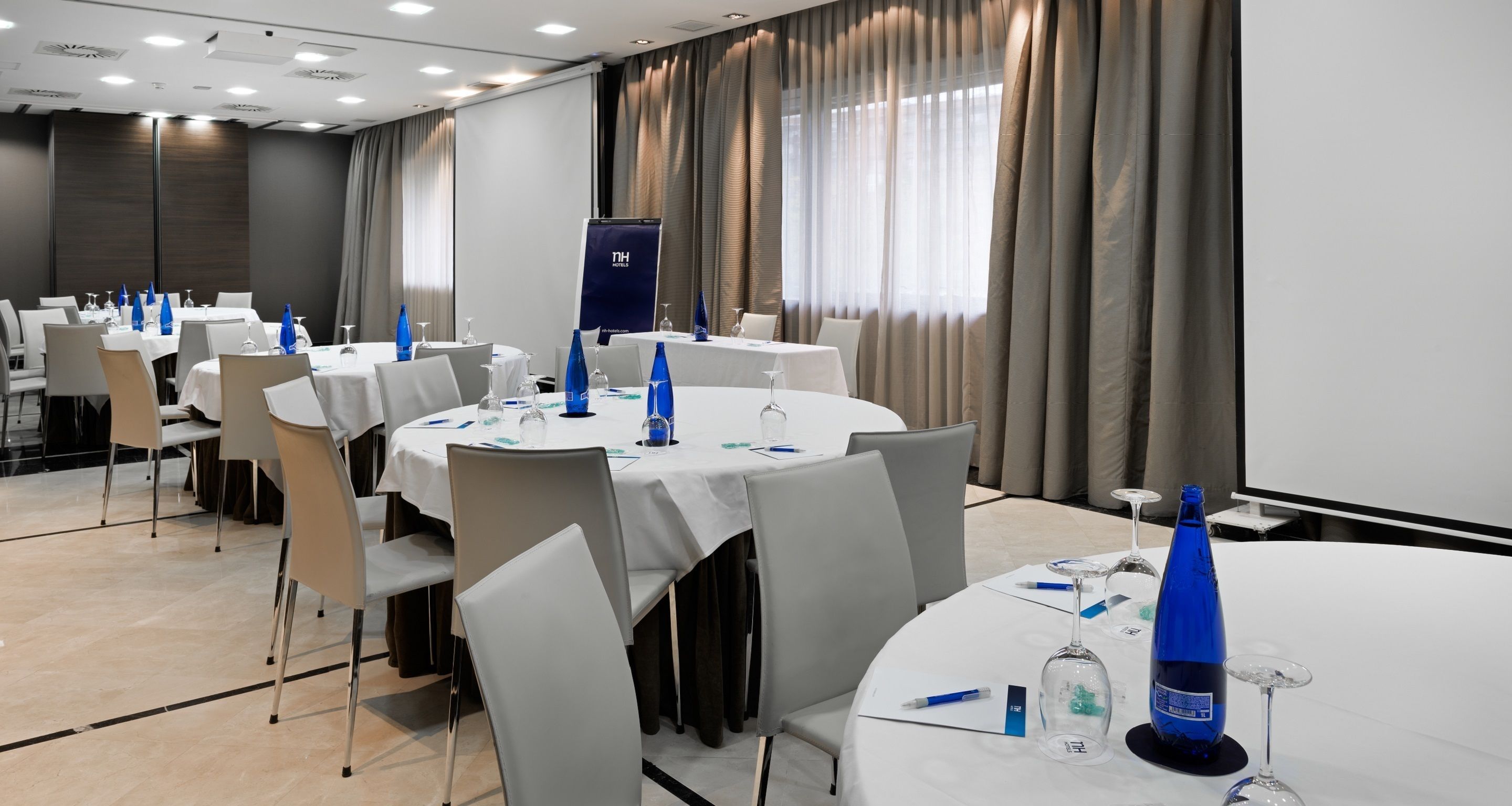 A conference room with round tables, white chairs, and blue water bottles.