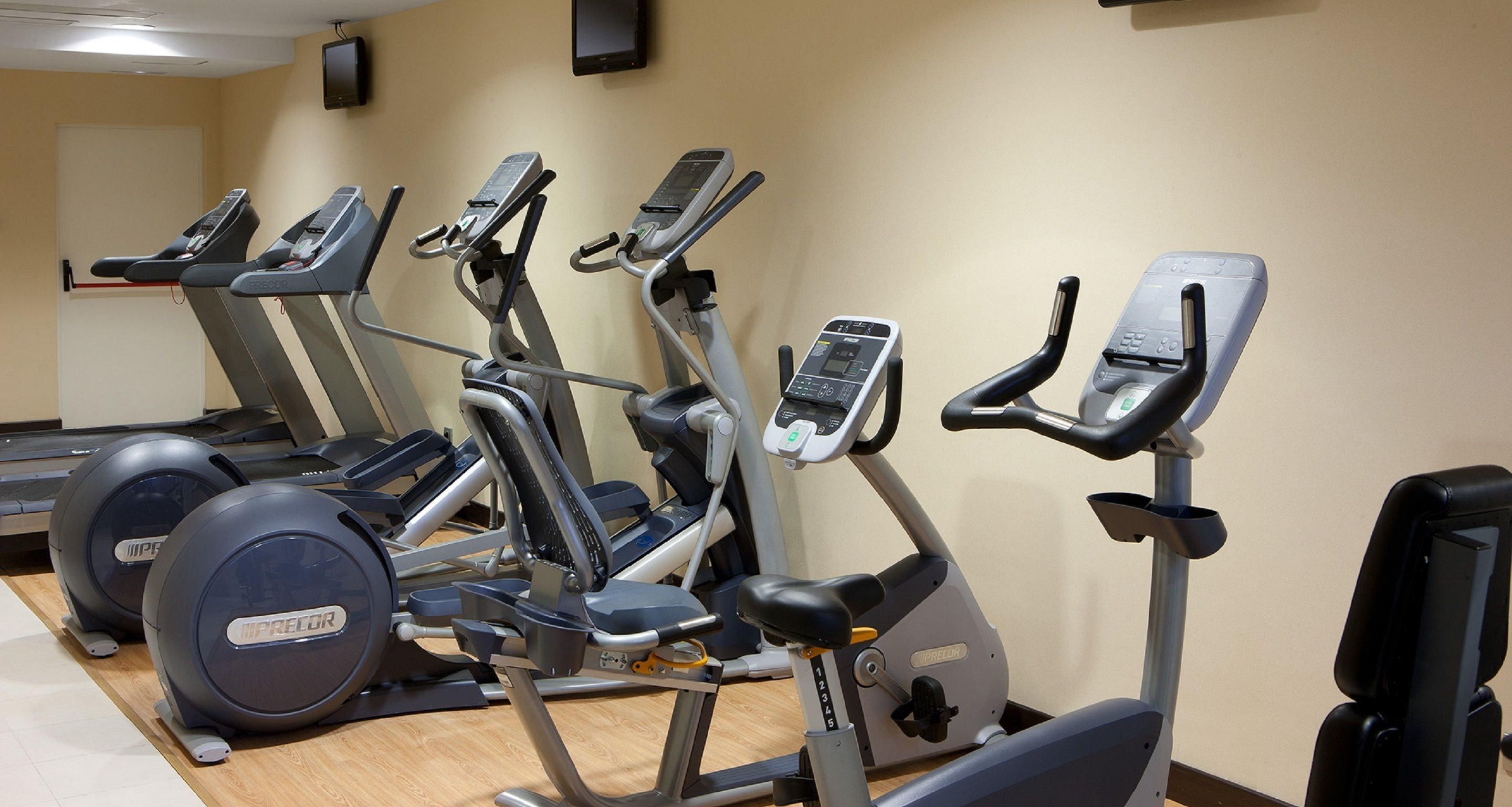 A gym with multiple exercise machines, including treadmills and elliptical trainers, arranged in a row.