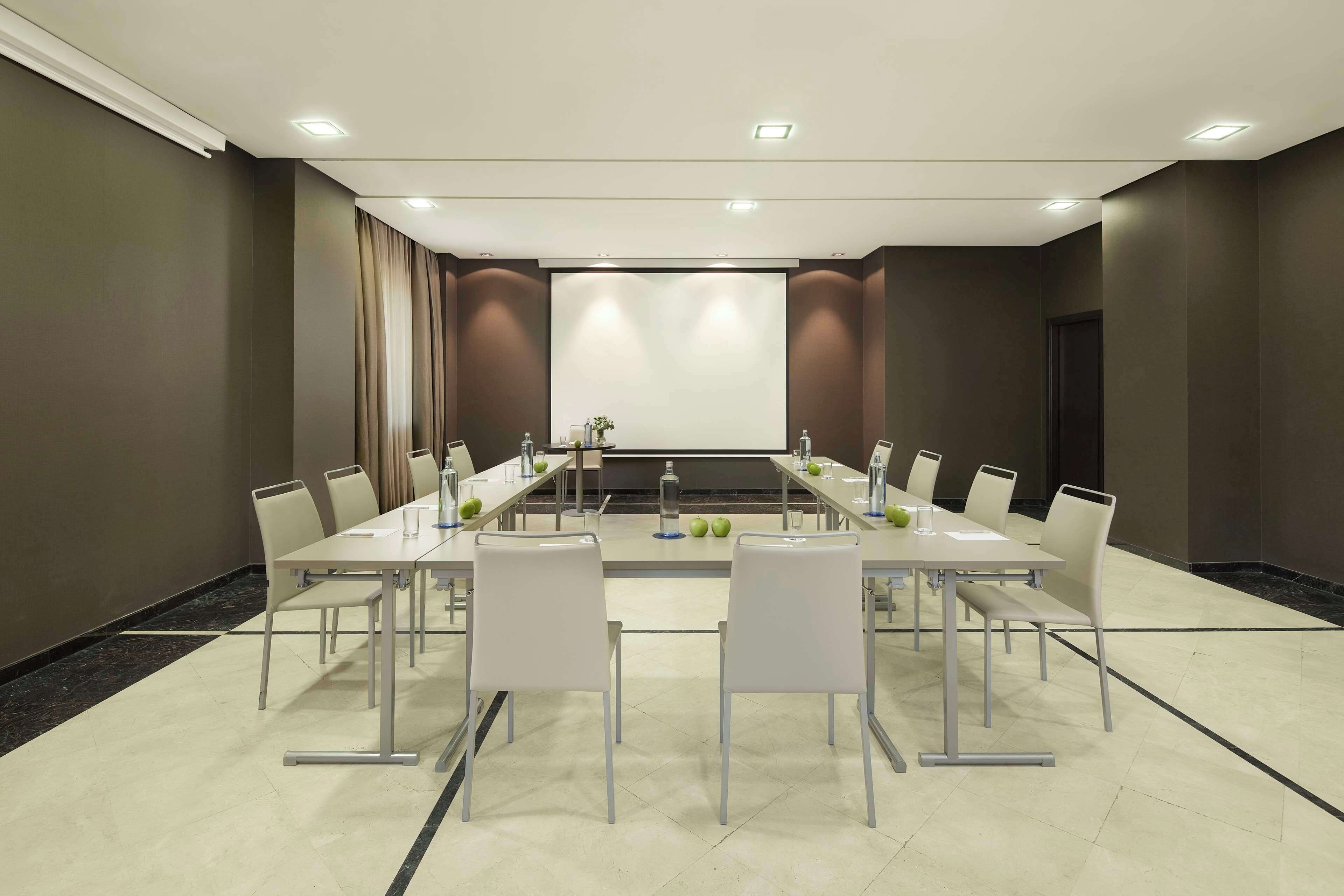 Une salle de conférence équipée d’une longue table, de chaises, d’un écran de projection et d’une petite table sur laquelle sont disposées des bouteilles d’eau et des pommes.