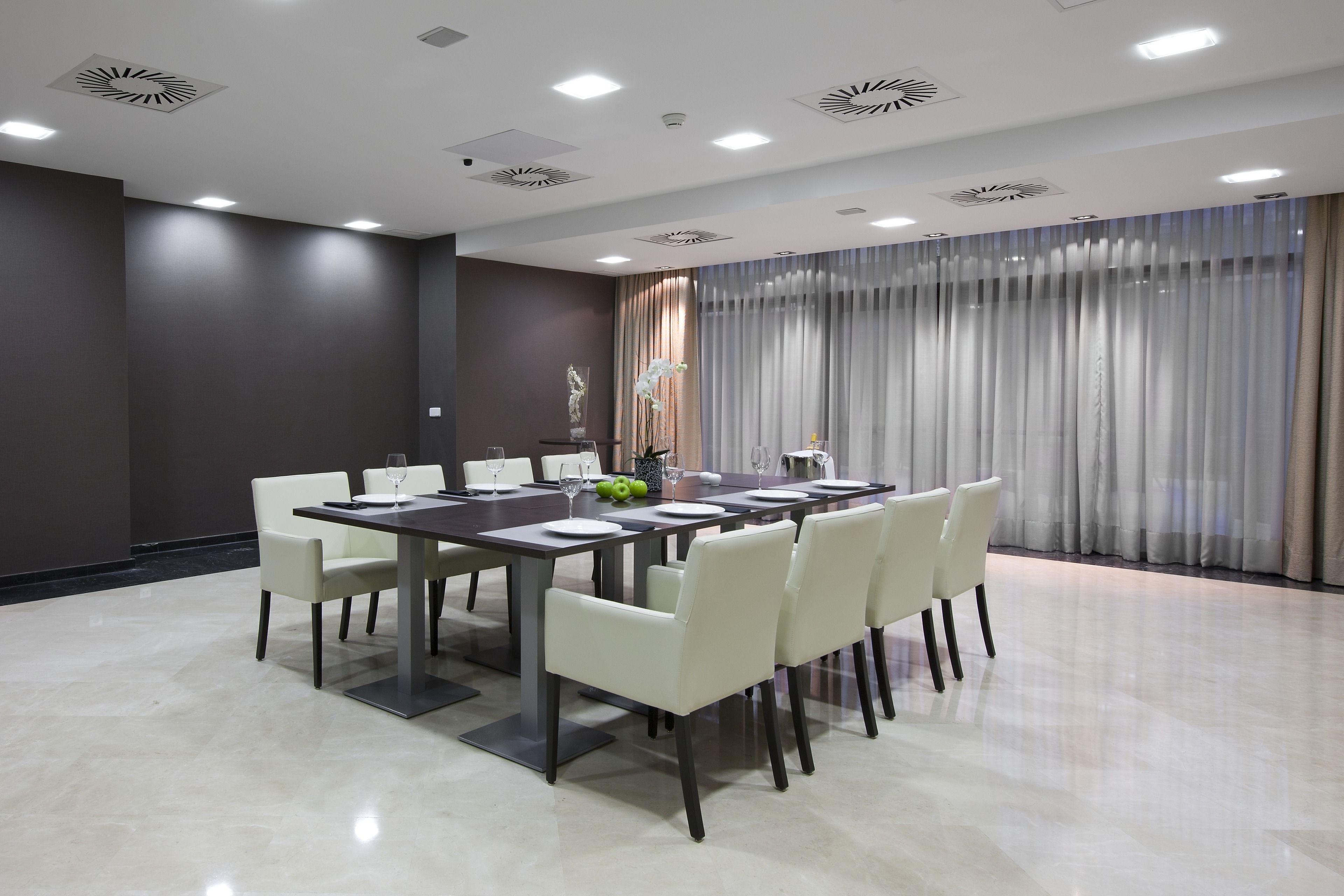 A conference room with a long table, white chairs, and a modern ceiling design.