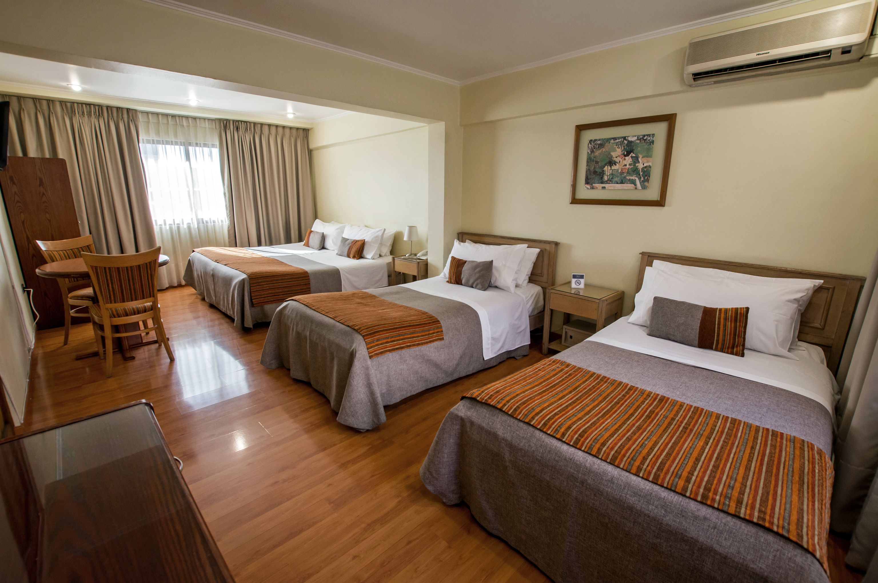 A hotel room with three beds, wooden furniture, and an air conditioning unit.