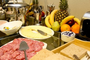 A buffet table with various food items including sliced cheese, cured meats, fruits, and bread. - RQ Central (Santiago)