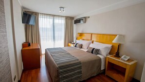 A hotel room with a bed, a TV mounted on the wall, a bedside table with a lamp and a phone, and a window with curtains. - RQ Central (Santiago)