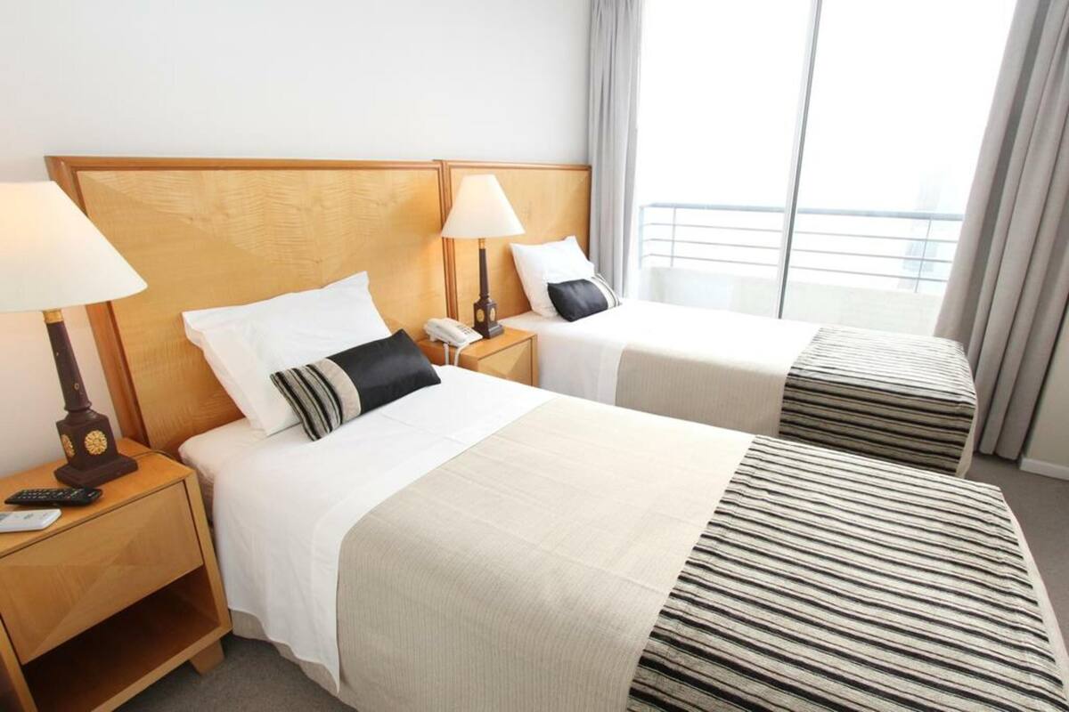 Ein Hotelzimmer mit zwei Betten, jeweils mit einem hölzernen Kopfstück, Nachttischlampen und einem Telefon.