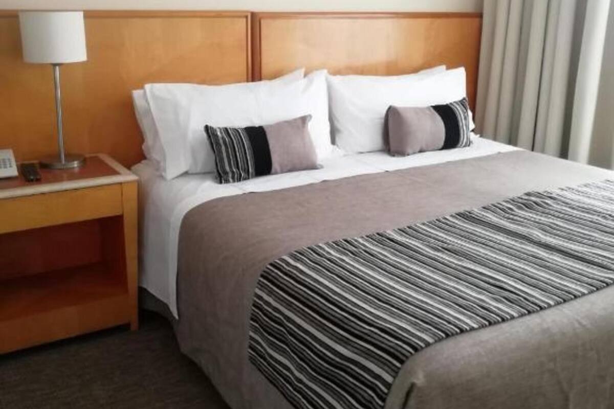 Ein Hotelzimmer mit Bett, Nachttisch, Lampe und einem Fenster mit Vorhängen.